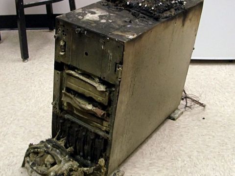 Ausgebrannter Server-Tower mit geschmolzenen Laufwerken auf einem Büroboden