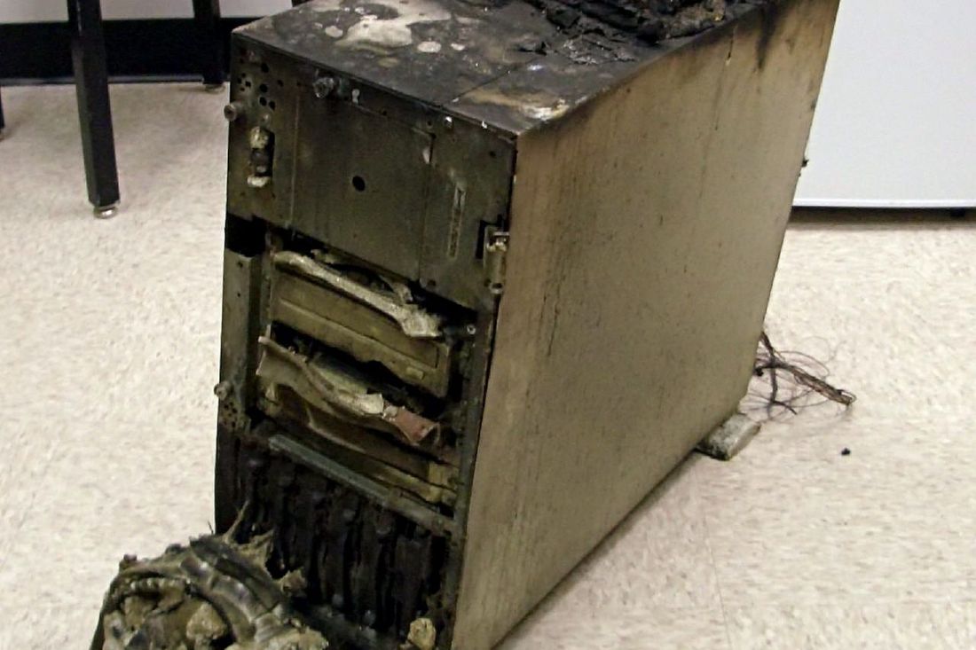 Ausgebrannter Server-Tower mit geschmolzenen Laufwerken auf einem Büroboden