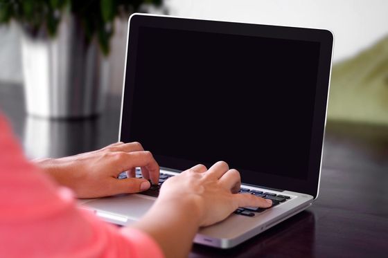Zwei Hände tippen auf der Tastatur eines silbernen Laptops mit dunklem Bildschirm