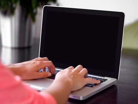 Zwei Hände tippen auf der Tastatur eines silbernen Laptops mit dunklem Bildschirm