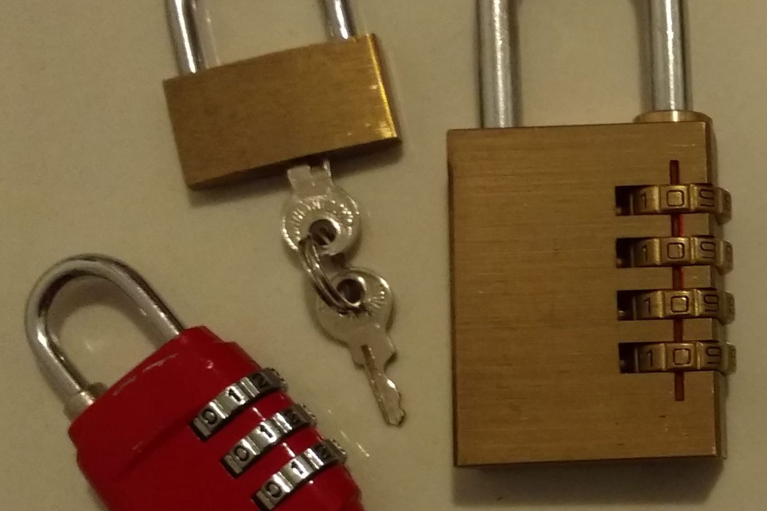 Drei Vorhängeschlösser, ein rotes Zahlenschloss und zwei aus Messing, eines mit Schlüsseln